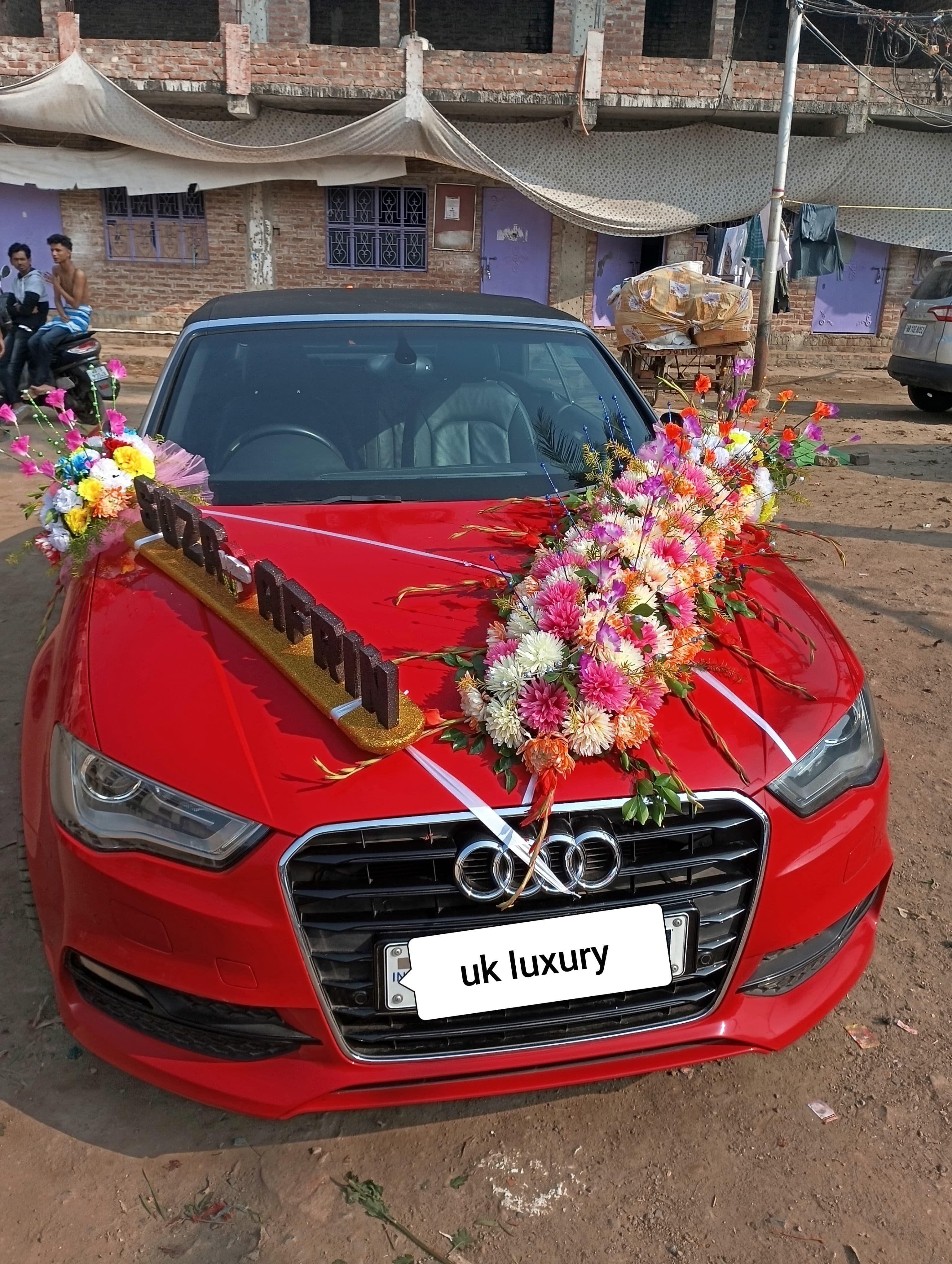 रंगीन फूलों और नेमप्लेट से सजी एक लाल ऑडी कार, शादी के लिए तैयार।